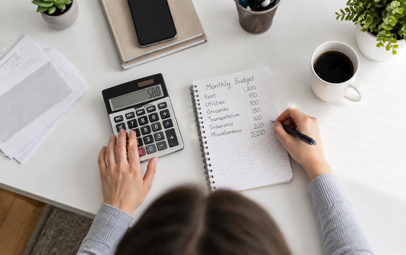 A person working through a monthly budget with a calculator and notebook