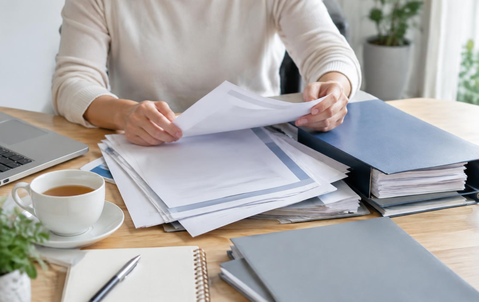 Hands sorting through policy documents and folders on a desk